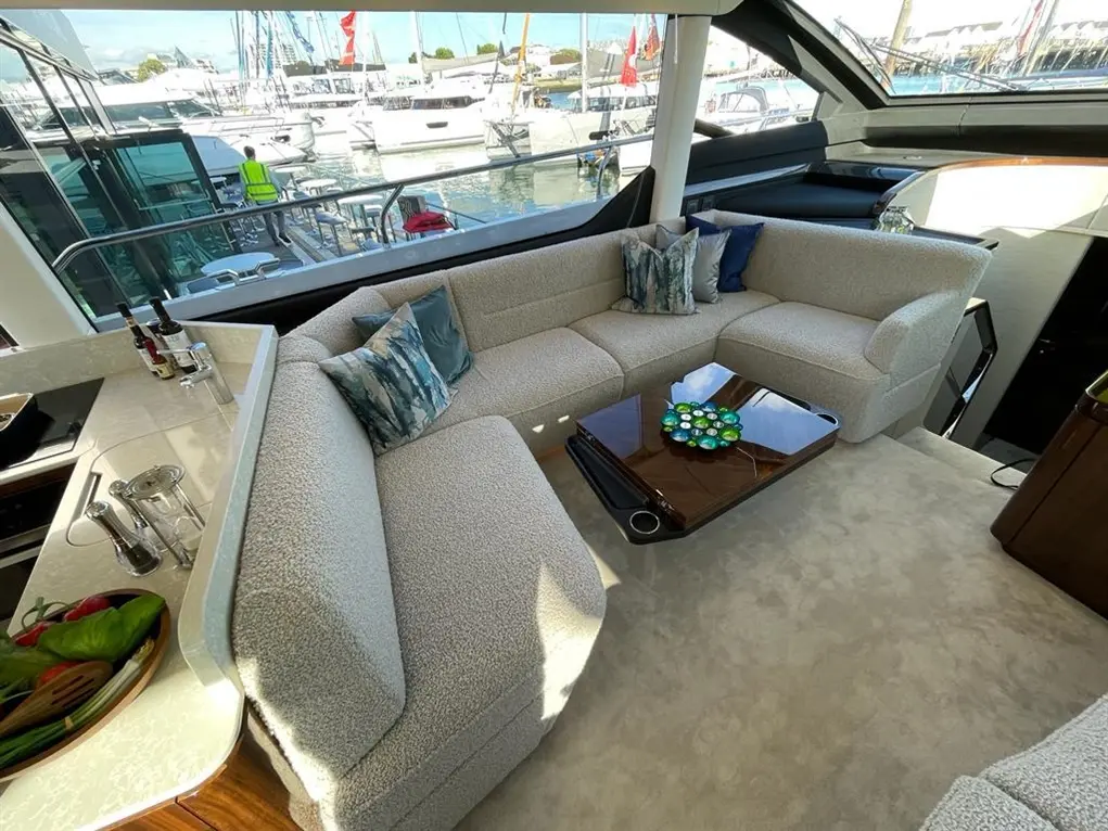Stylish yacht interior featuring a plush L-shaped sofa, decorative cushions, a coffee table, and a view of moored boats.